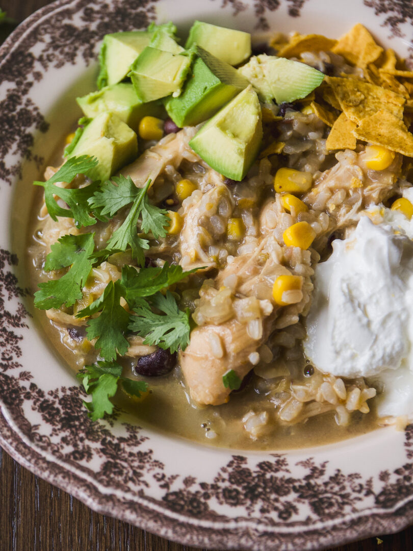 A bowl of chicken, rice, and bean soup topped with avocado, tortilla chips, sour cream, and cilantro.