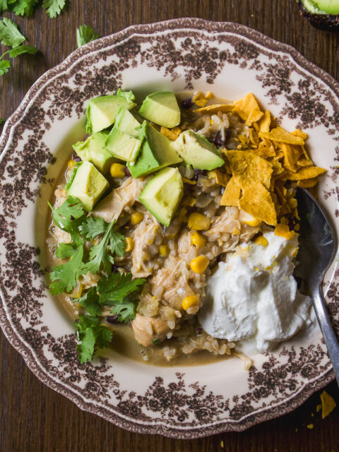 A bowl of chicken, rice, corn, and black bean stew topped with avocado, tortilla chips, cilantro, and a dollop of sour cream.