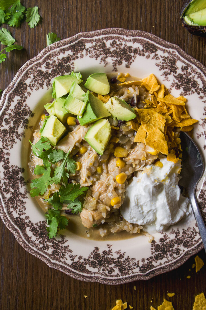 A bowl of chicken, rice, corn, and black bean stew topped with avocado, tortilla chips, cilantro, and a dollop of sour cream.