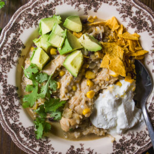 A bowl of chicken and rice soup topped with diced avocado, crushed tortilla chips, cilantro, and a dollop of sour cream.