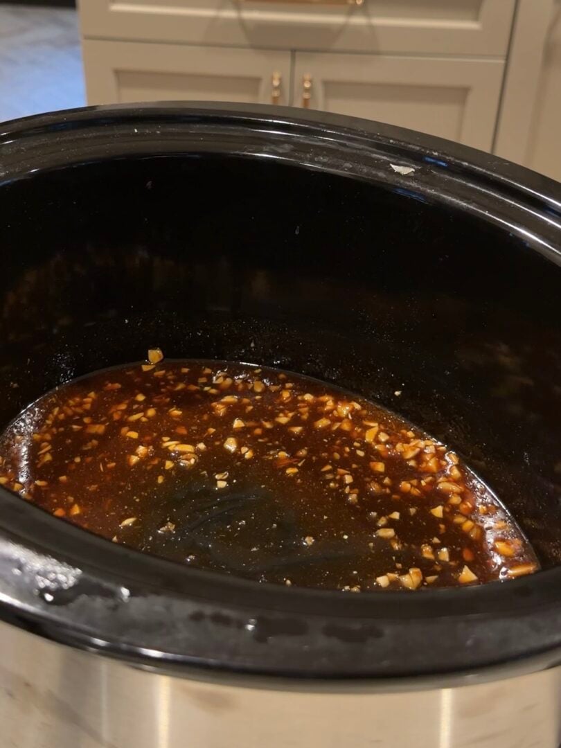 A dark, savory sauce with minced garlic cooking in a slow cooker.