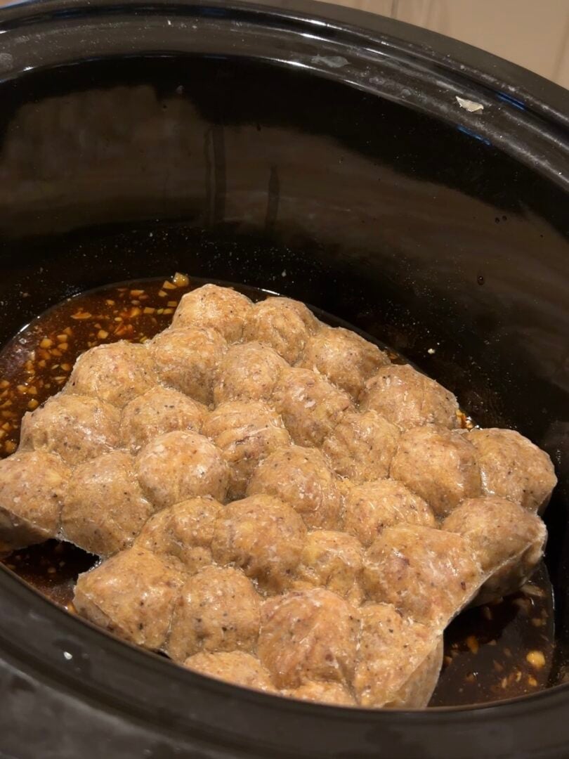 A block of frozen meatballs in a slow cooker filled with brown sauce.