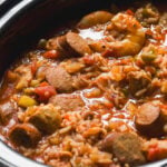 A slow cooker filled with shrimp and sliced sausage jambalaya with rice, tomatoes, and vegetables.