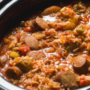 A slow cooker filled with shrimp and sliced sausage jambalaya with rice, tomatoes, and vegetables.