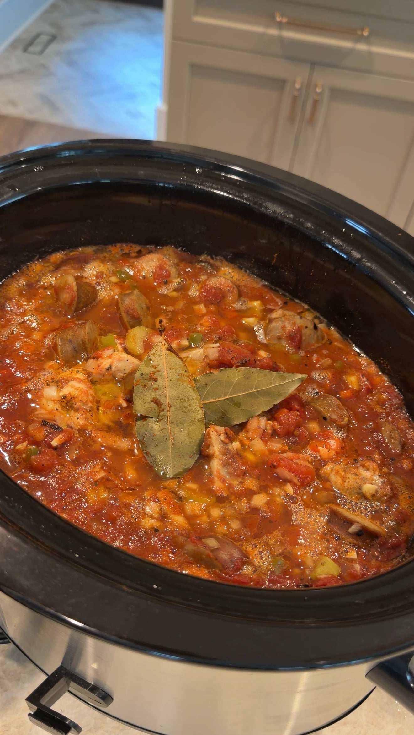 Tomato-based stew with sliced sausage and two bay leaves cooking in a slow cooker.