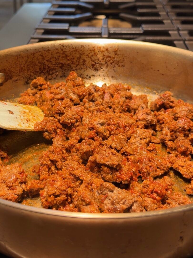 Ground meat cooking in a stainless steel skillet with a wooden spatula.