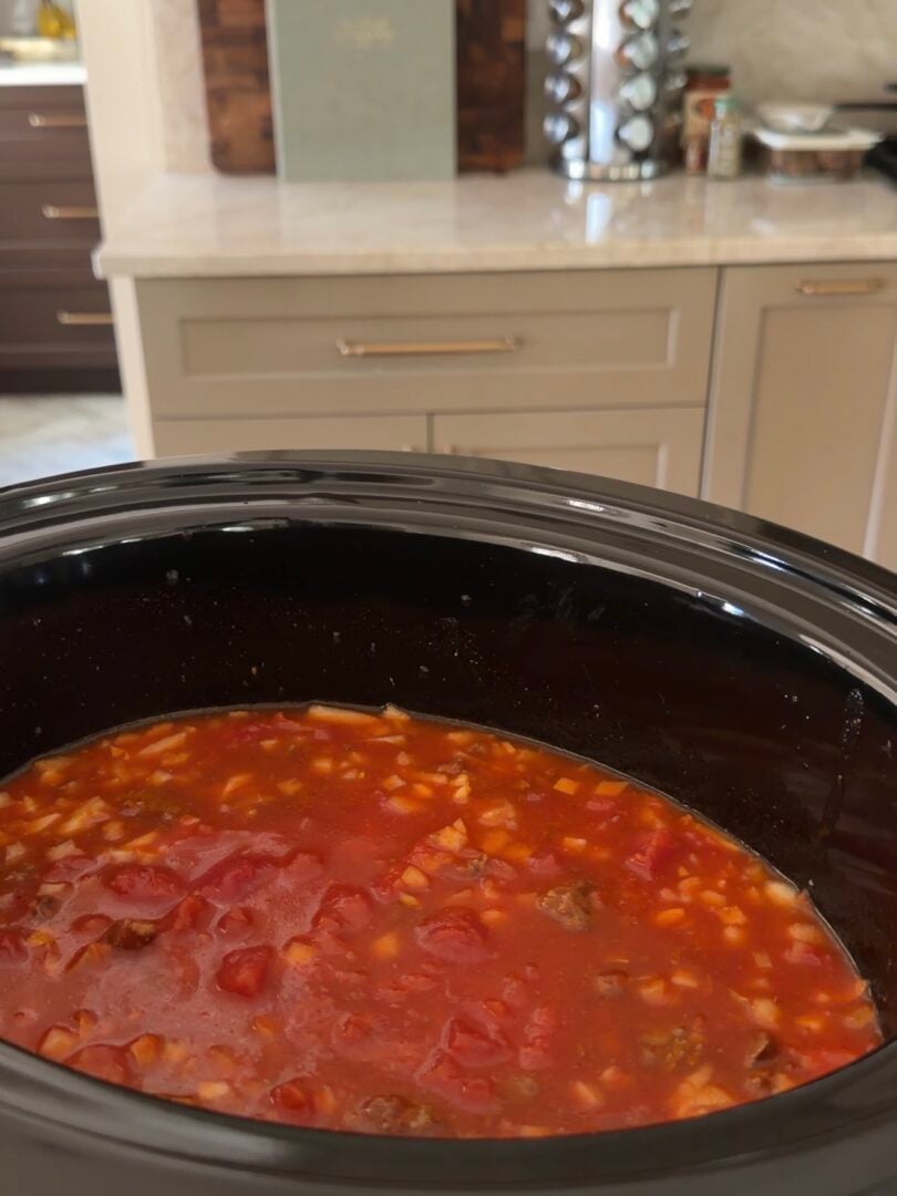 A black slow cooker filled with a chunky red tomato and vegetable stew.