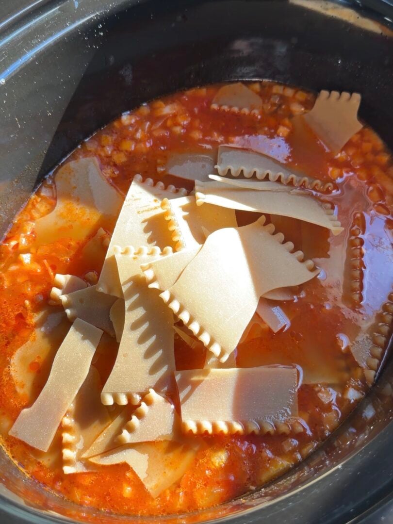 Broken pieces of lasagna noodles floating in tomato-based sauce inside a slow cooker.