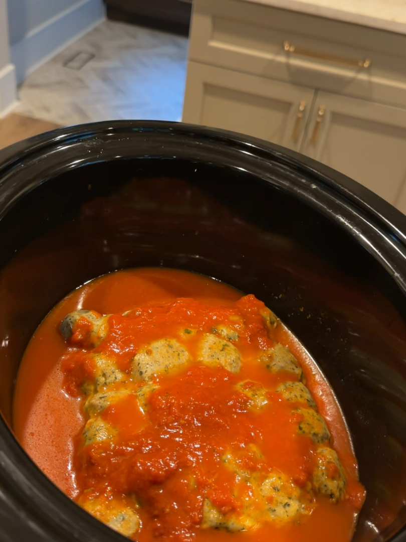 Meatballs and orzo cooking in tomato sauce inside a slow cooker.