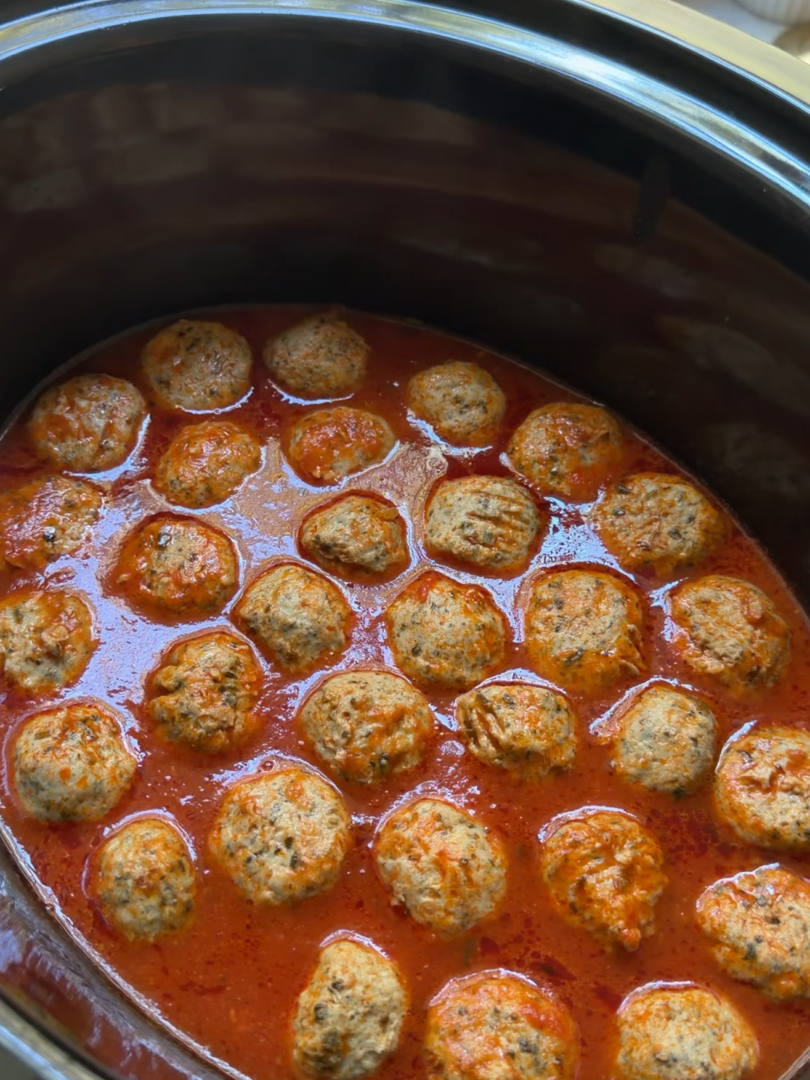 Meatballs and orzo simmering in red sauce inside a slow cooker.