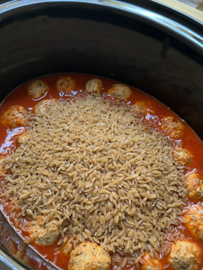 Crockpot meatballs and orzo pasta simmer in a slow cooker filled with red tomato sauce.