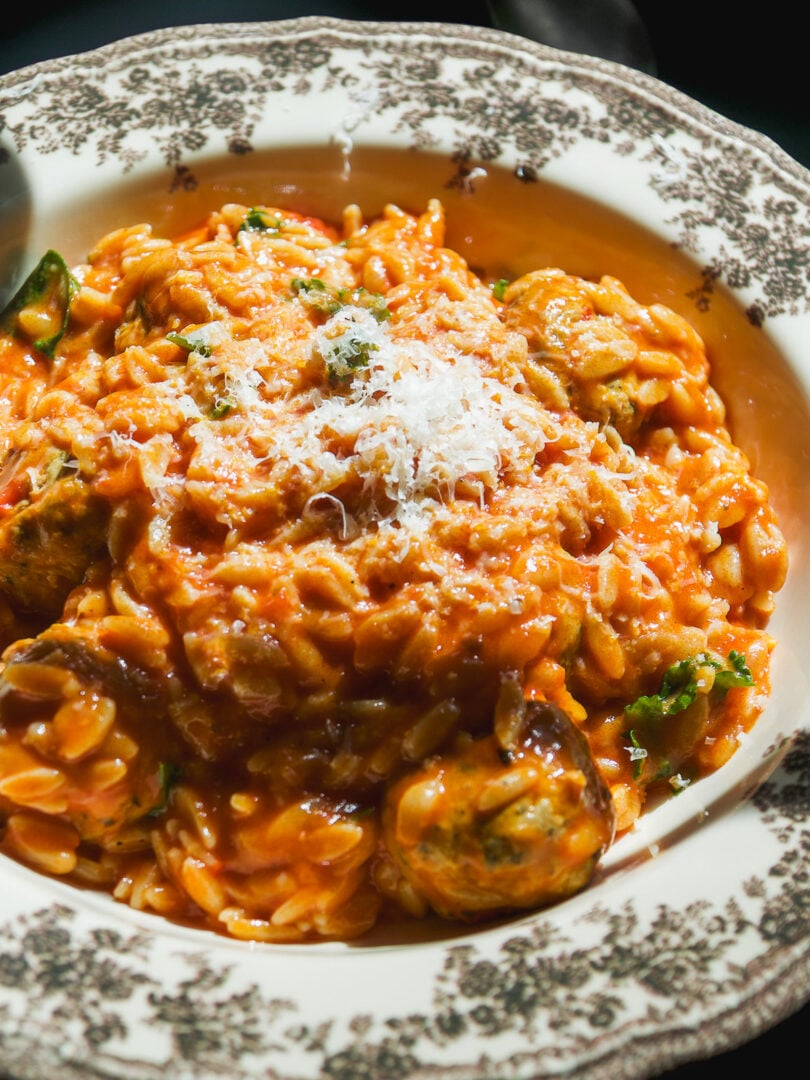 A bowl of crockpot meatballs and orzo in a creamy tomato sauce, topped with grated parmesan cheese.