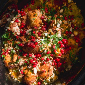 Slow cooker chicken and rice topped with pomegranate seeds, pine nuts, and fresh herbs.