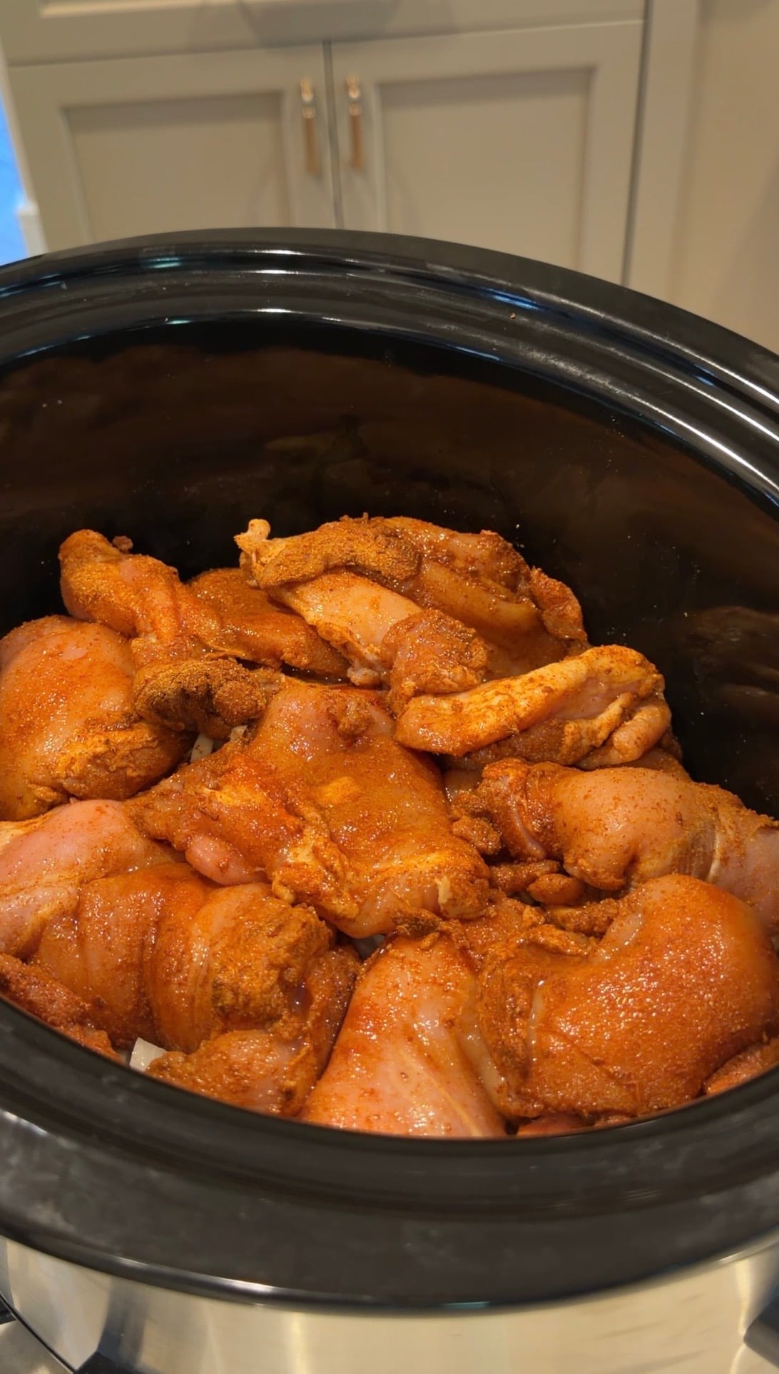 Raw chicken thighs coated in red seasoning in a slow cooker.