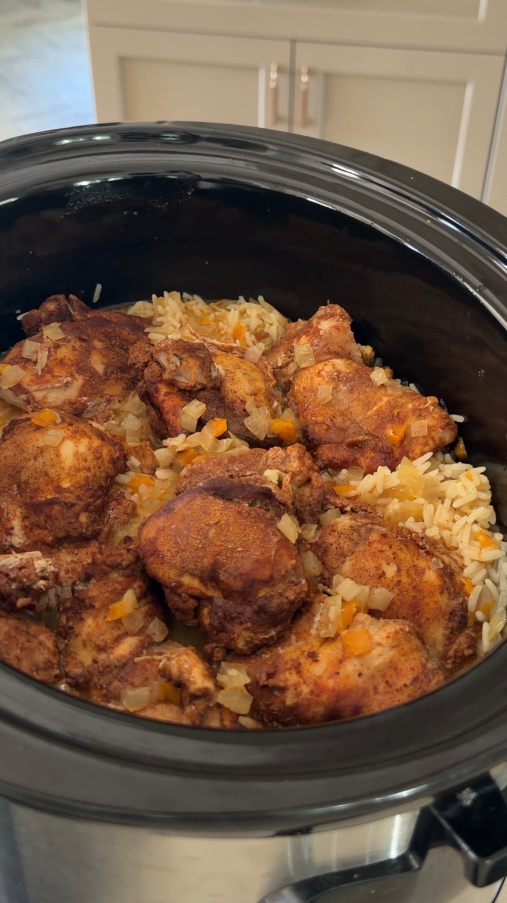 Slow cooker filled with seasoned chicken thighs and rice with diced vegetables.