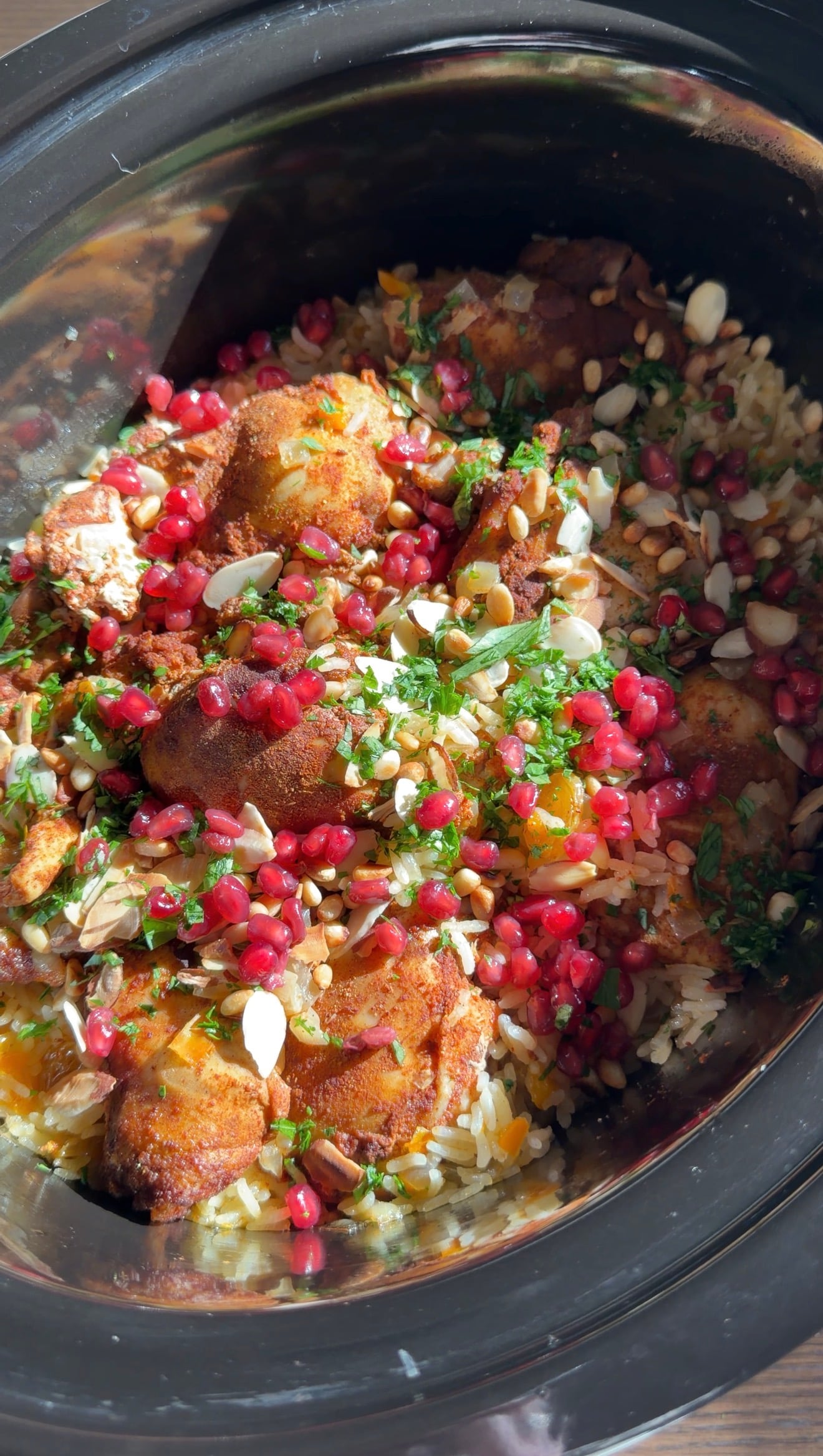 Chicken and rice in a slow cooker, topped with pomegranate seeds, sliced almonds, and fresh herbs.