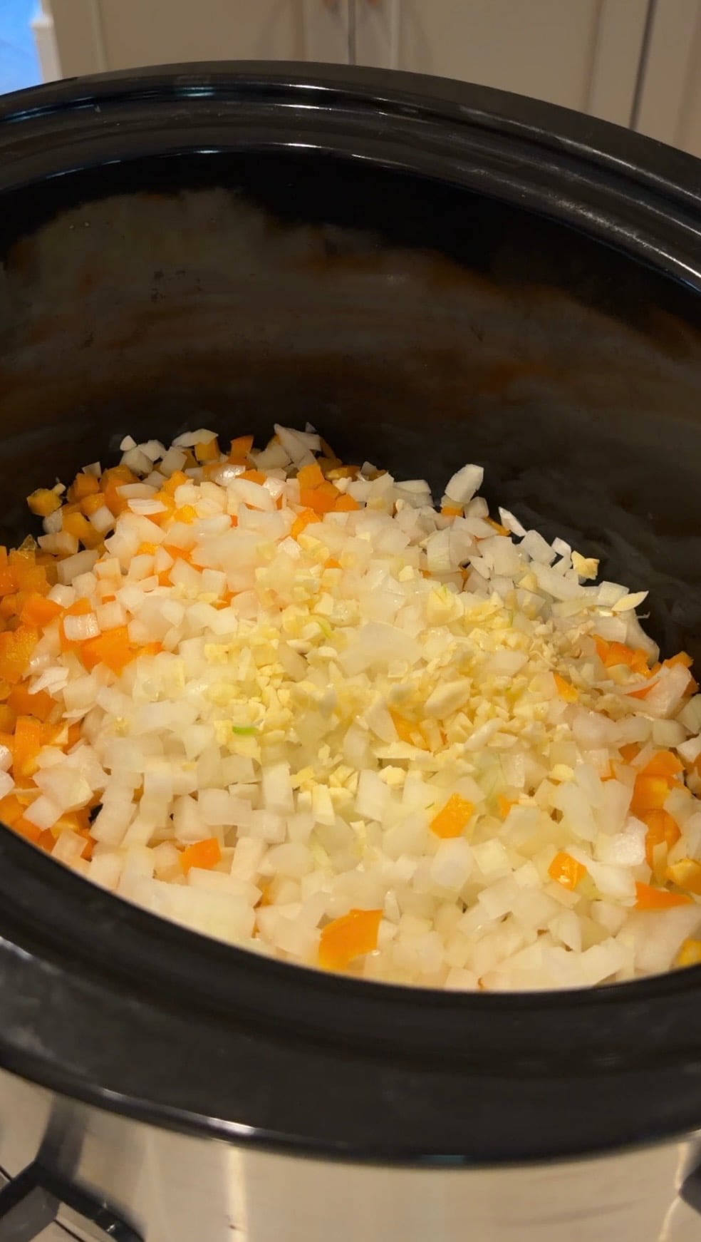 Chopped onions, orange bell peppers, and minced garlic in a black slow cooker.