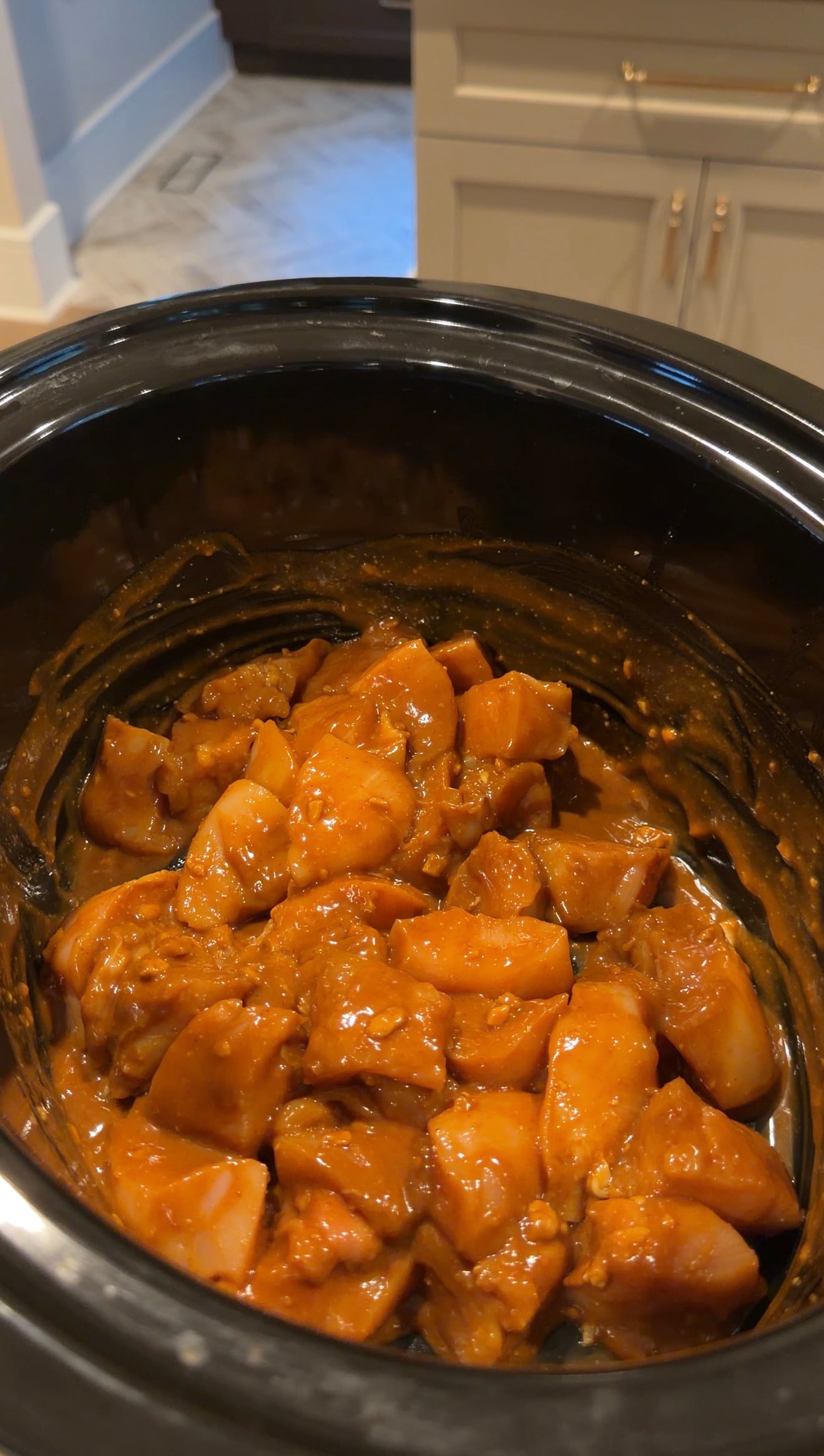 Raw chicken chunks coated in a thick, orange-brown sauce inside a slow cooker.