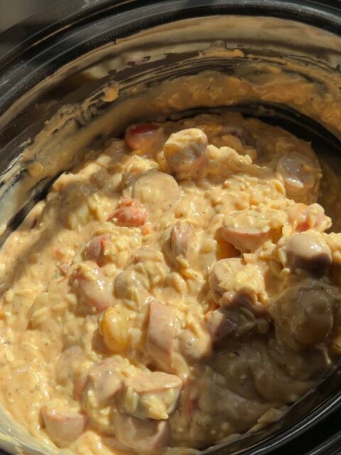 A creamy dish with sliced sausages in a slow cooker.