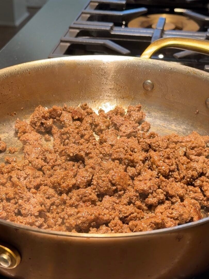 Ground meat browning in a metal skillet on a stovetop.
