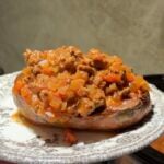 A baked sweet potato topped with a savory ground meat and tomato sauce on a patterned plate.