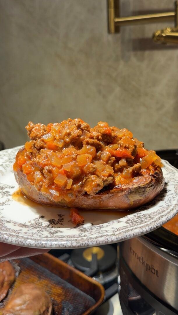 A baked sweet potato topped with a savory ground meat and tomato sauce on a patterned plate.