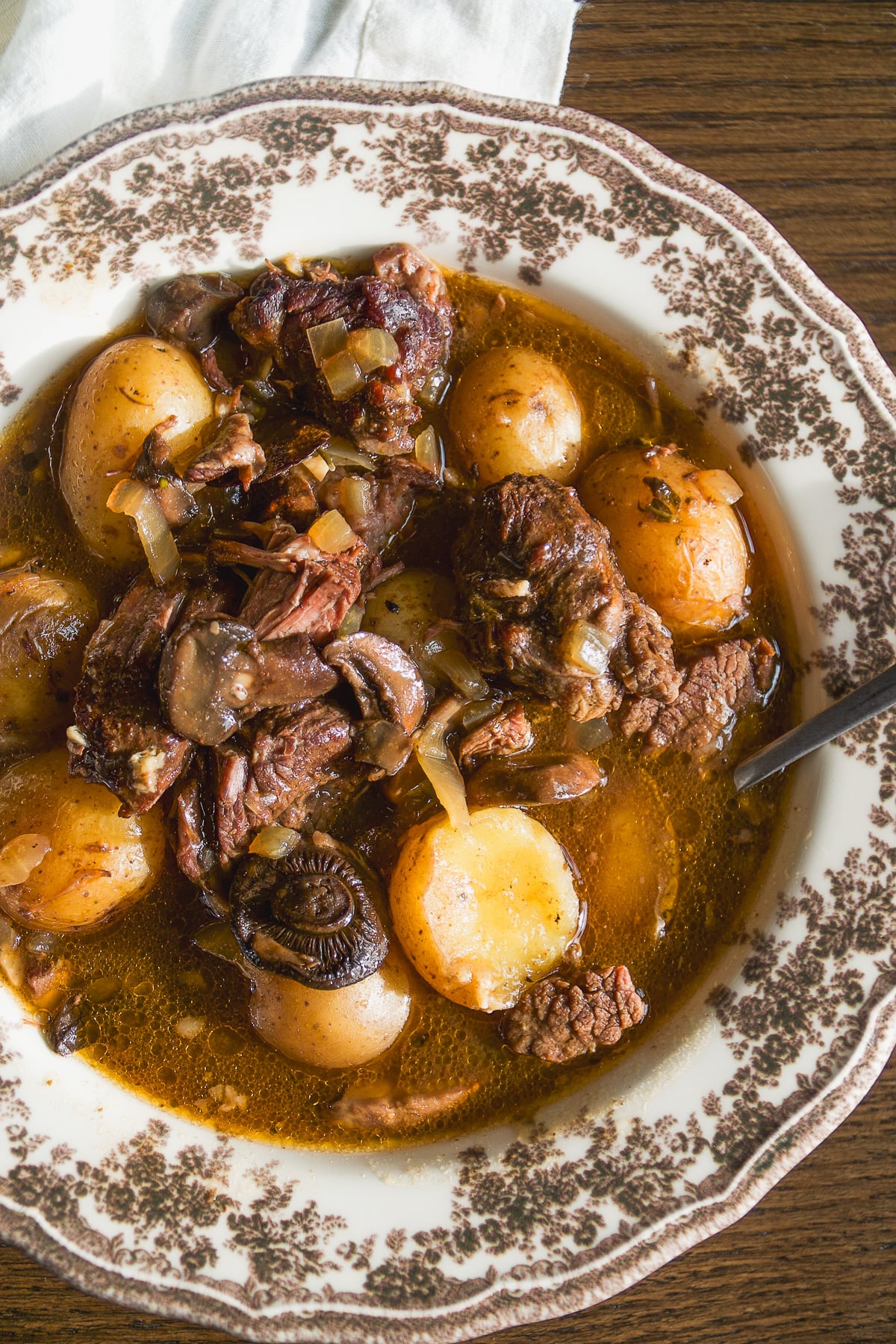 A bowl of beef stew with potatoes and mushrooms in a patterned bowl.