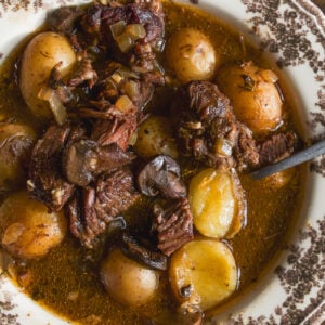 A bowl of beef stew with chunks of meat, mushrooms, and whole baby potatoes in a dark broth.