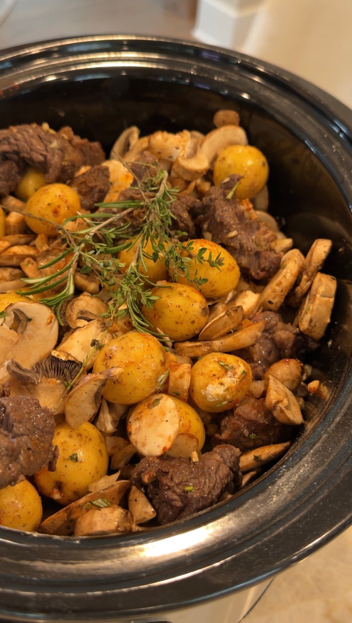Slow cooker crockpot steak and potatoes beef stew with yellow potatoes, sliced mushrooms, and fresh sprigs of thyme.