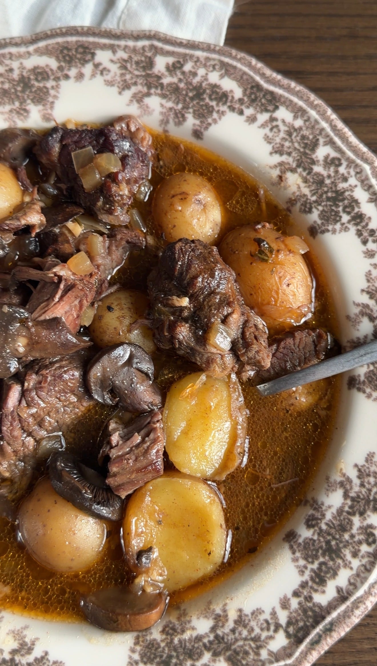 A bowl of crockpot steak and potatoes with mushrooms in a patterned bowl.