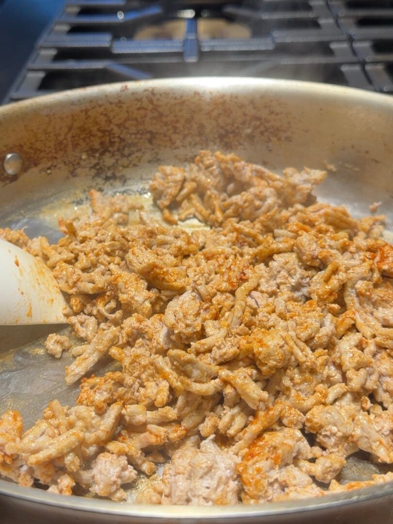 Ground meat browning in a metal skillet with a spatula.