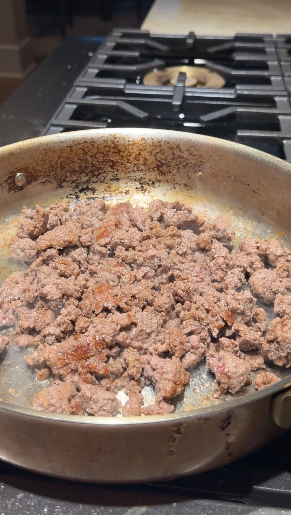Ground meat browning in a stainless steel skillet on a stovetop.