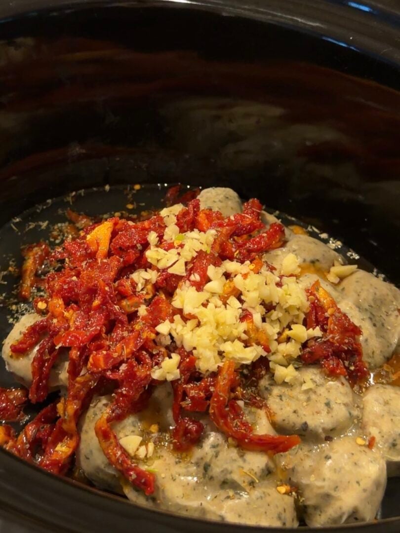 Slow cooker filled with gnocchi topped with sun-dried tomatoes and chopped garlic.