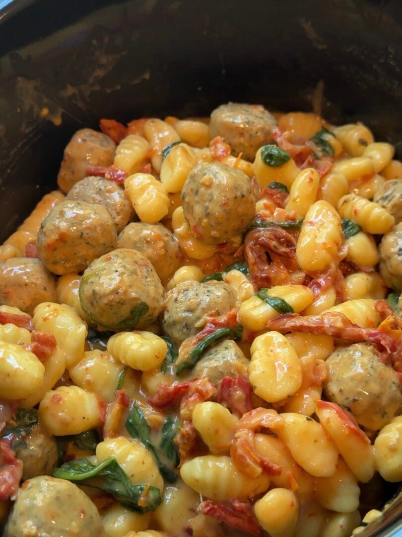 Gnocchi with meatballs, sun-dried tomatoes, and spinach in a creamy sauce, served in a slow cooker.