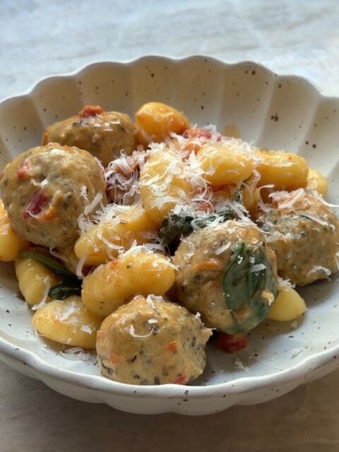 A scalloped bowl filled with gnocchi and meatballs, garnished with grated cheese.