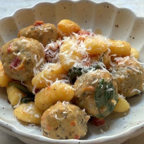 A scalloped bowl filled with gnocchi and meatballs, garnished with grated cheese.
