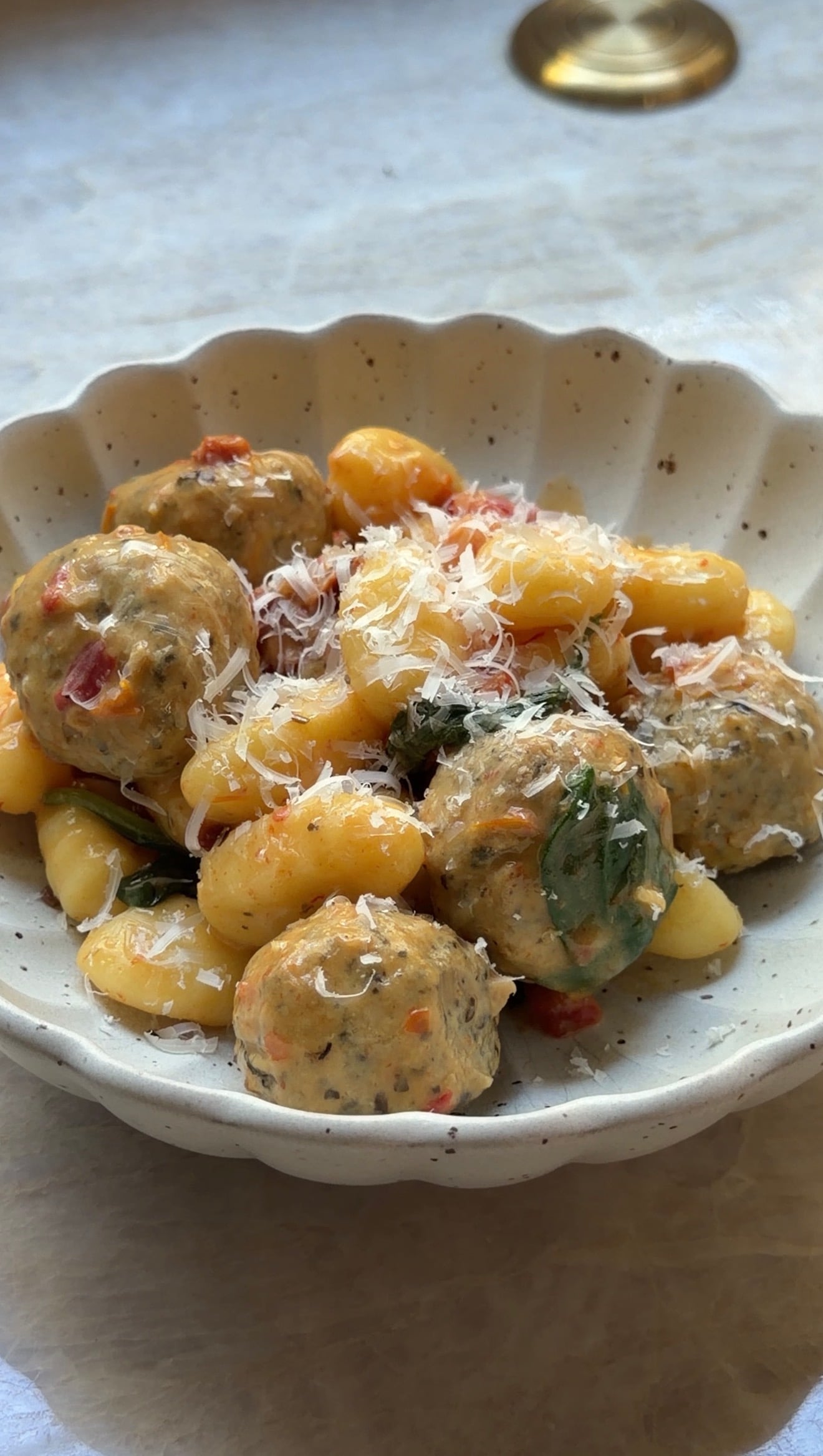 A scalloped bowl filled with gnocchi and meatballs, garnished with grated cheese.