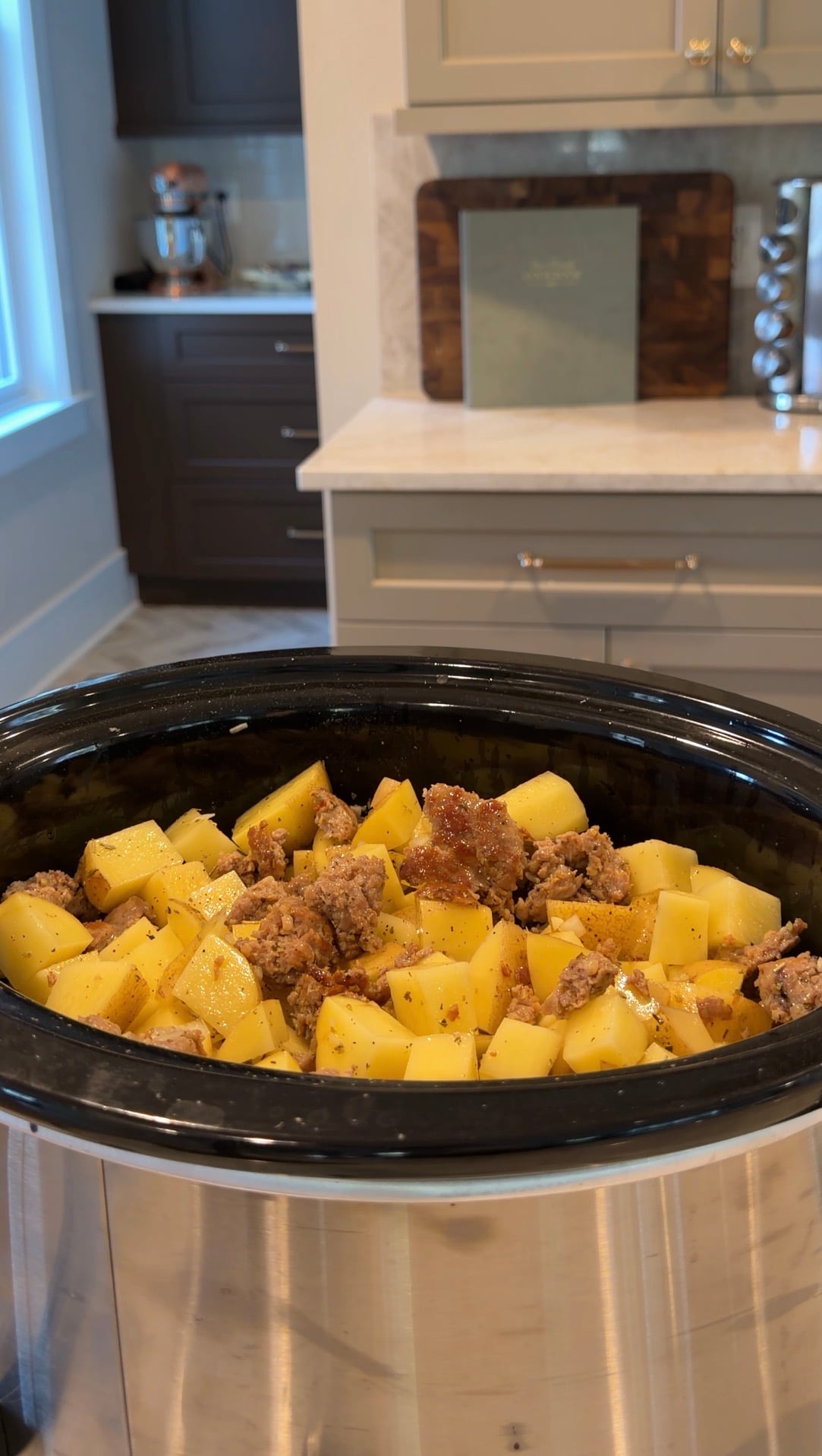 A slow cooker filled with diced potatoes and crumbles of cooked meat.