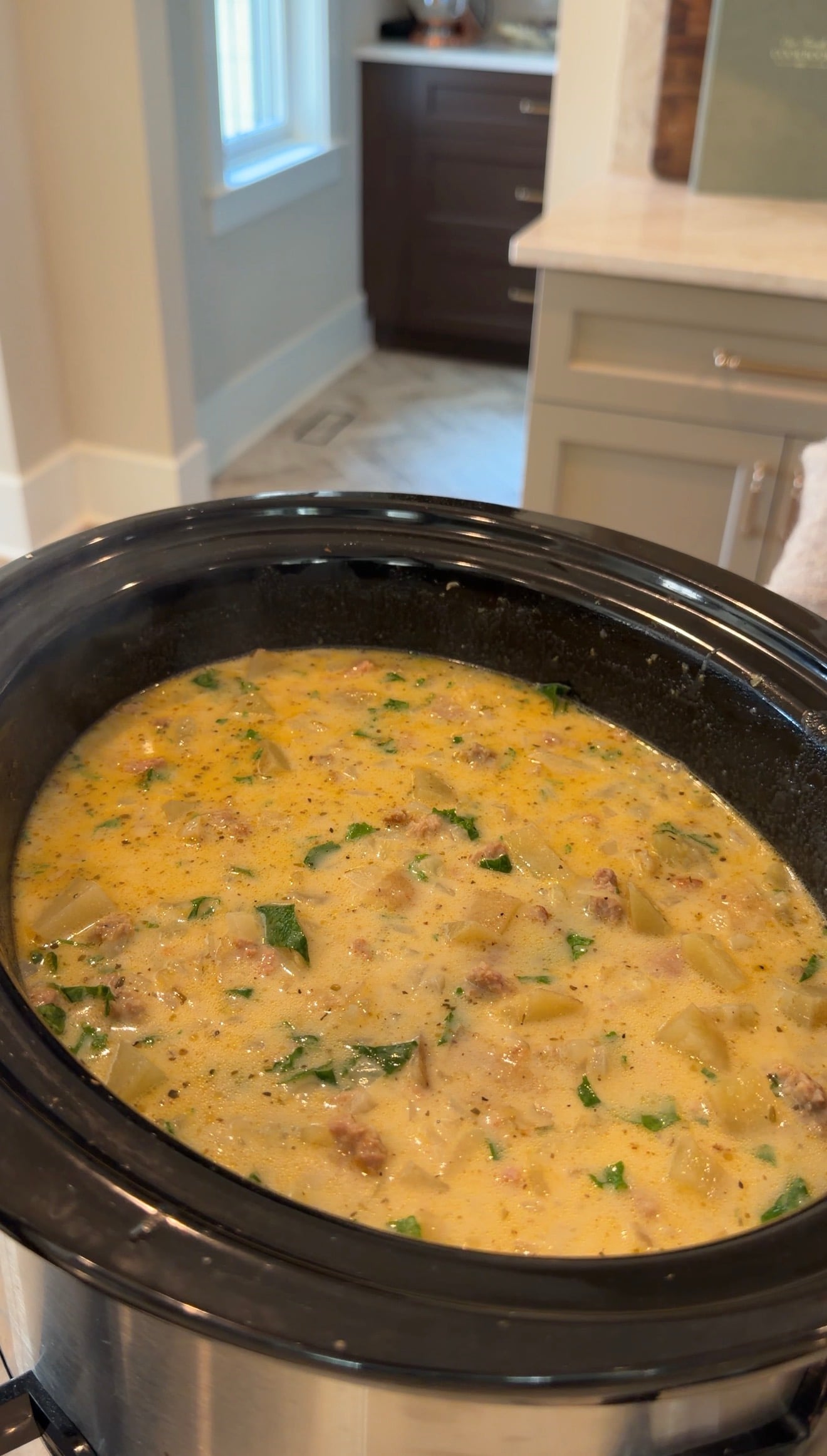 Creamy potato and sausage soup with greens cooking in a slow cooker.