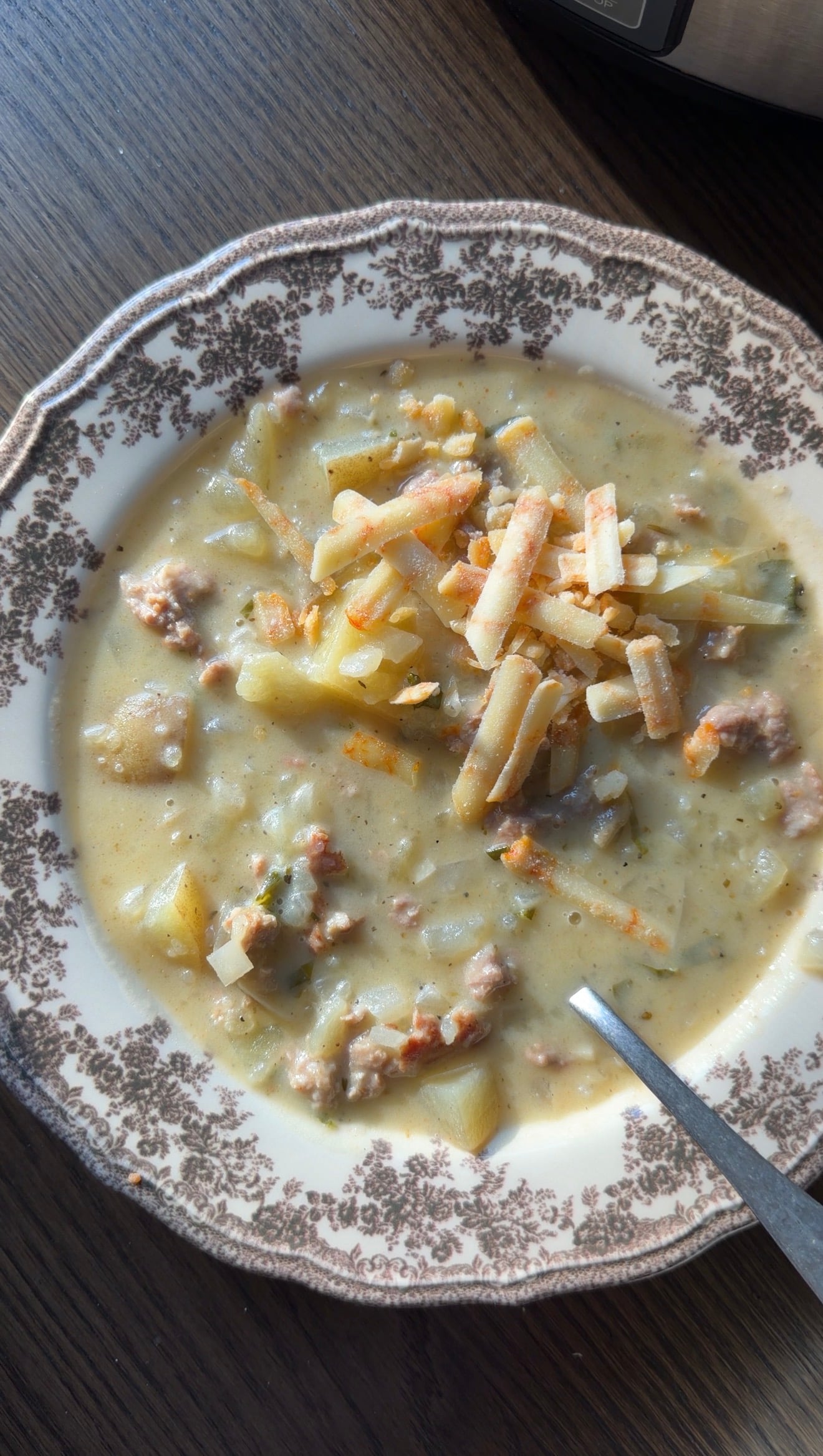 A bowl of creamy potato and sausage soup topped with shredded cheese and a spoon.