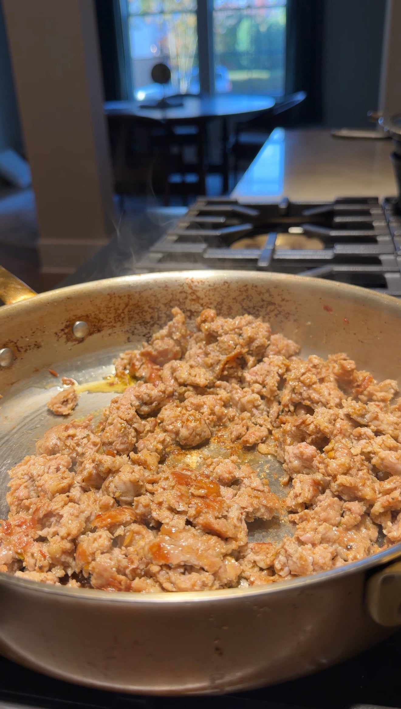 Ground meat browning in a stainless steel skillet on a stovetop.