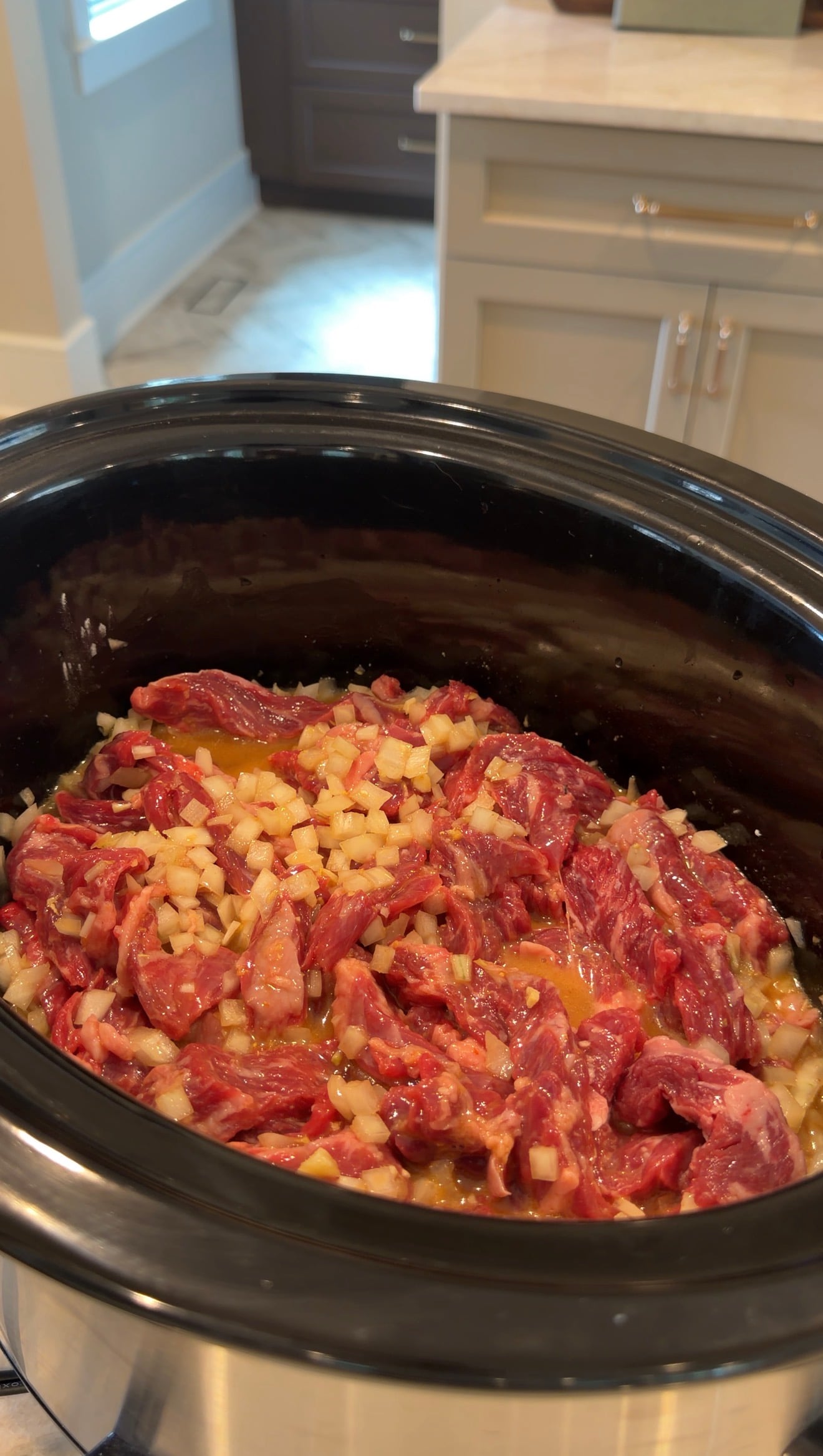 Raw strips of beef topped with diced onions in a slow cooker.