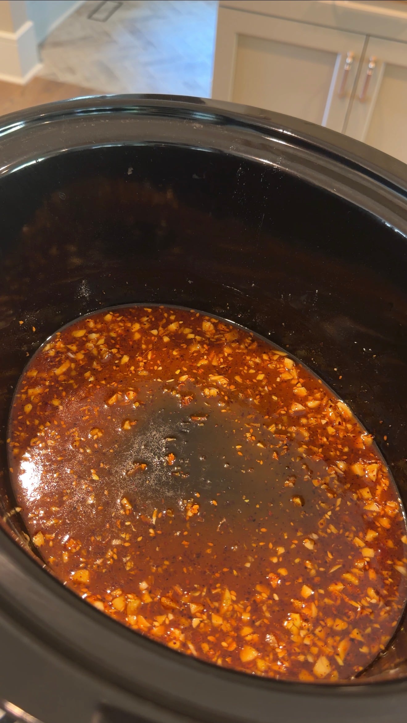 A dark, thin sauce with minced garlic and red pepper flakes cooking in a slow cooker.