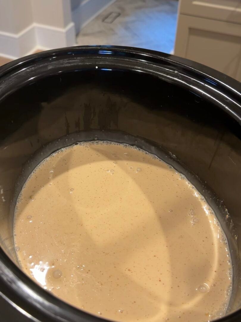 A light tan liquid with small bubbles cooking inside a black slow cooker insert.