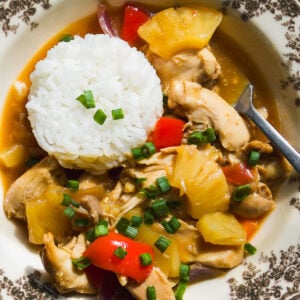 A bowl of chicken and pineapple stir-fry served with a scoop of white rice, garnished with green onions.