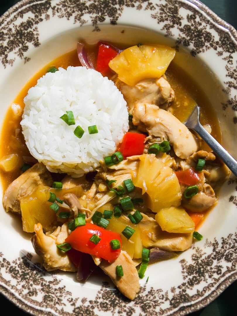 A bowl of chicken and pineapple stir-fry served with a scoop of white rice, garnished with green onions.