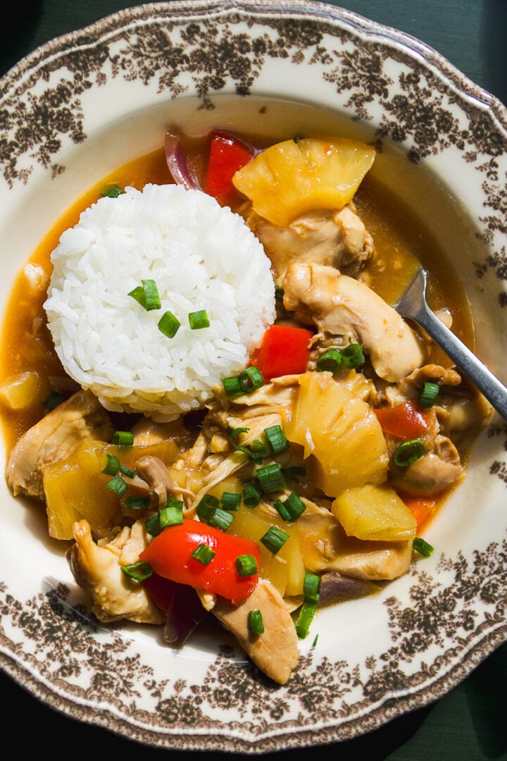 A bowl of chicken and pineapple stir-fry served with a scoop of white rice, garnished with green onions.